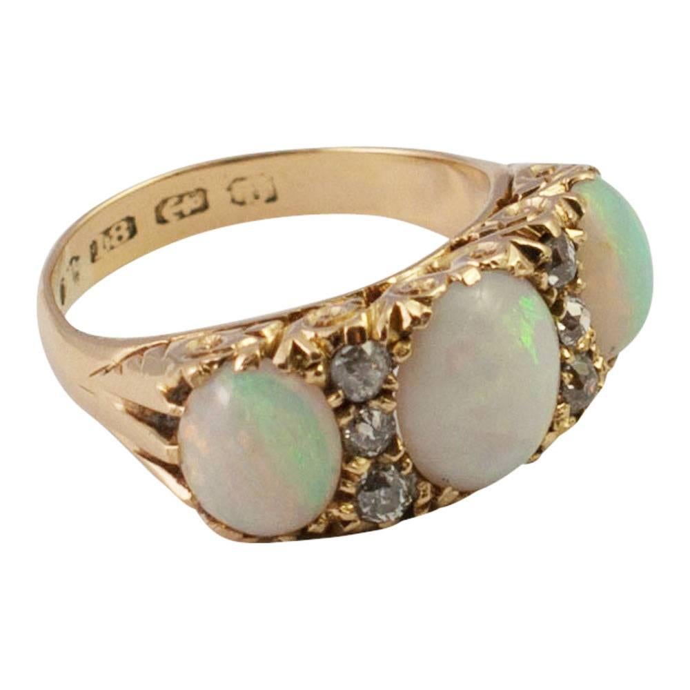 Three stone opal and diamond Victorian ring in 18ct gold;  a lovely example of a late Victorian opal ring set with 3 harlequin opals, each separated by a row of three Old European cut diamonds in a carved and scrolled mount.  Hallmarked 18ct gold