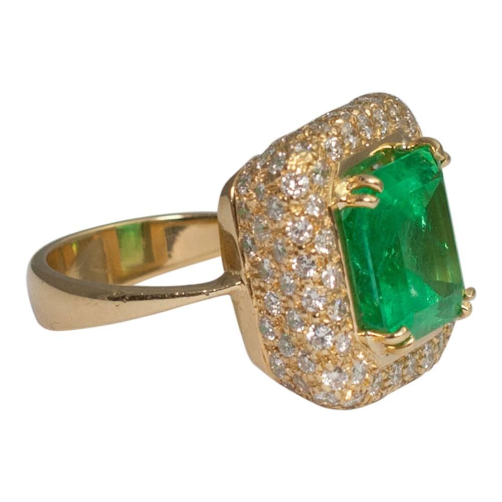 Vivid green 7.32ct emerald and diamond ring; the emerald is double claw set on top of a spectacular mount covered in 4 rows of brilliant cut diamonds around the sides totalling 2.10ct.  It has a wide gold band, stamped 750.  Weight 11.9gms.  Finger