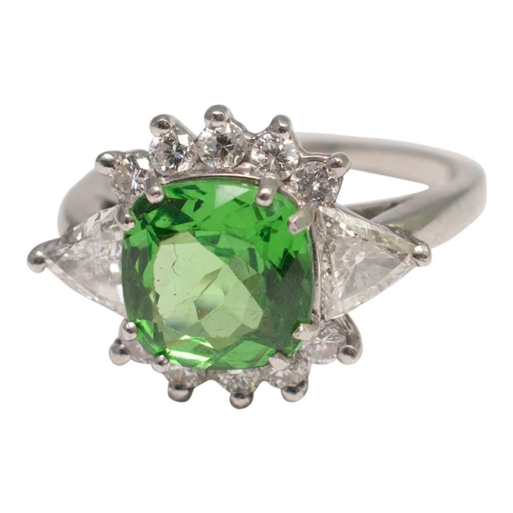 Tsavorite and diamond ring; the cushion cut tsavorite weighs 3.05ct and is a bright green colour, full of fire and brilliance.  It is flanked by two trillion diamonds and 10 brilliant cut diamonds weighing 1.05ct.  This is a gorgeous statement ring