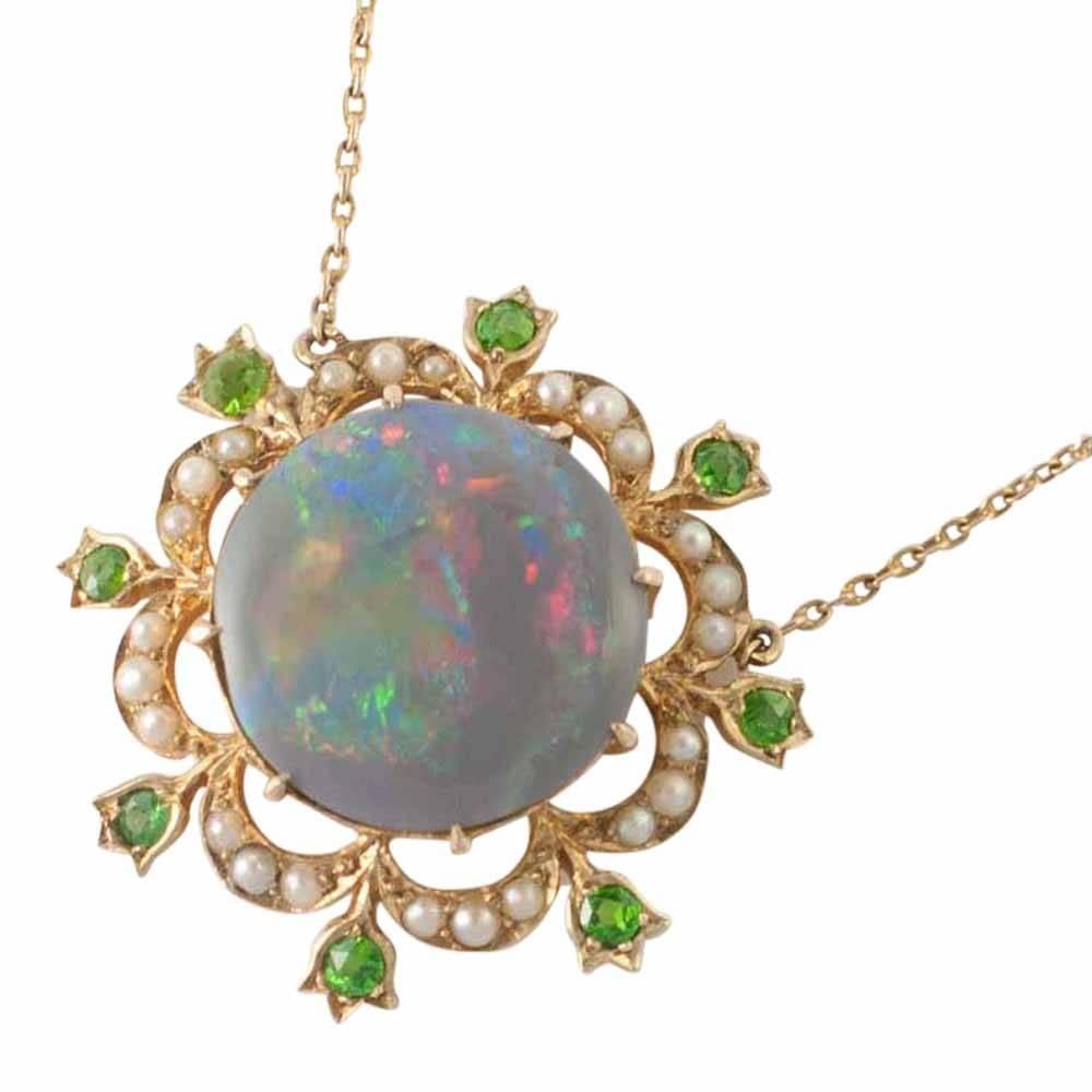 Edwardian black opal pendant; the opal has a full range of colours with flashes of red, yellow, green and blue.  It is surrounded by a border of split pearls and an outer row of demantoid garnets set in tulip mounts.  It has a fixed chain from links