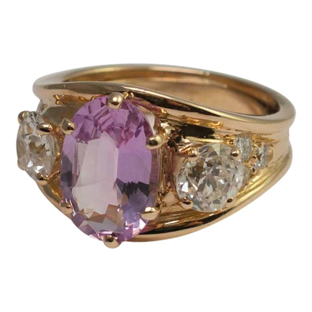 Oval mixed cut pink topaz weighing 3ct set with two Old European cut diamonds each weighing 0.77ct in a trilogy ring.  There are a further 6 brilliant cut diamonds, three on either side, totalling 0.24ct which add embellishment to the ring.  The