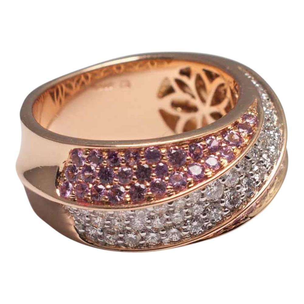 Pink sapphire and diamond band ring mounted in warm rose gold tones; the ring is formed of 2 tapered rows of pavé set pink sapphires with a tapered row of pavé set diamonds in between them in the form of a half hoop. The reeded design continues