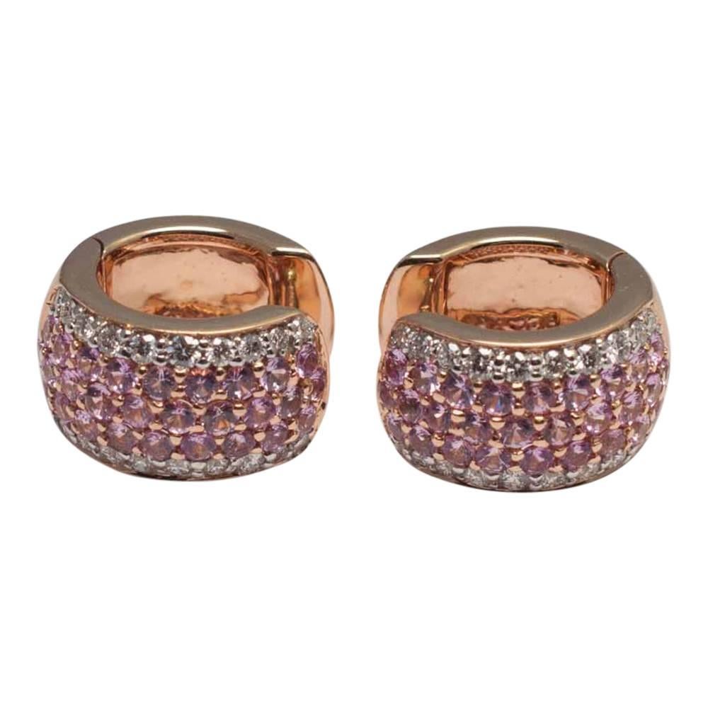 A small pair of pink sapphire and diamond hooped earrings formed of two rows of brilliant cut white diamonds and three rows of pink sapphires in between.  Mounted in warm tones of rose gold, these pretty earrings wrap around the lobe of the ear and