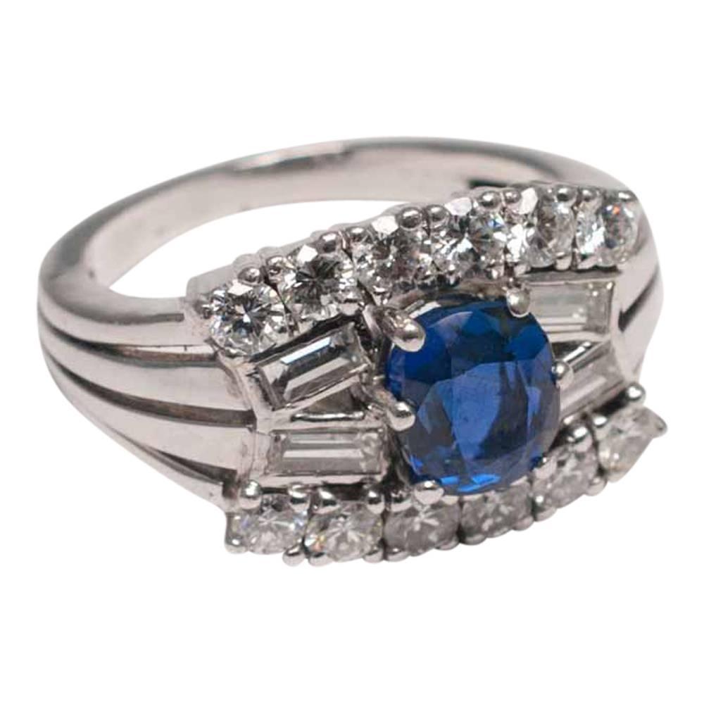 Unusual sapphire and diamond mid century ring; the oval sapphire weighs 1.25ct and is set with four baguette diamonds and two rows of brilliant cut diamonds. The shoulders are formed of 4 white gold bands which blend into the shank. Weight 9.8gms. 