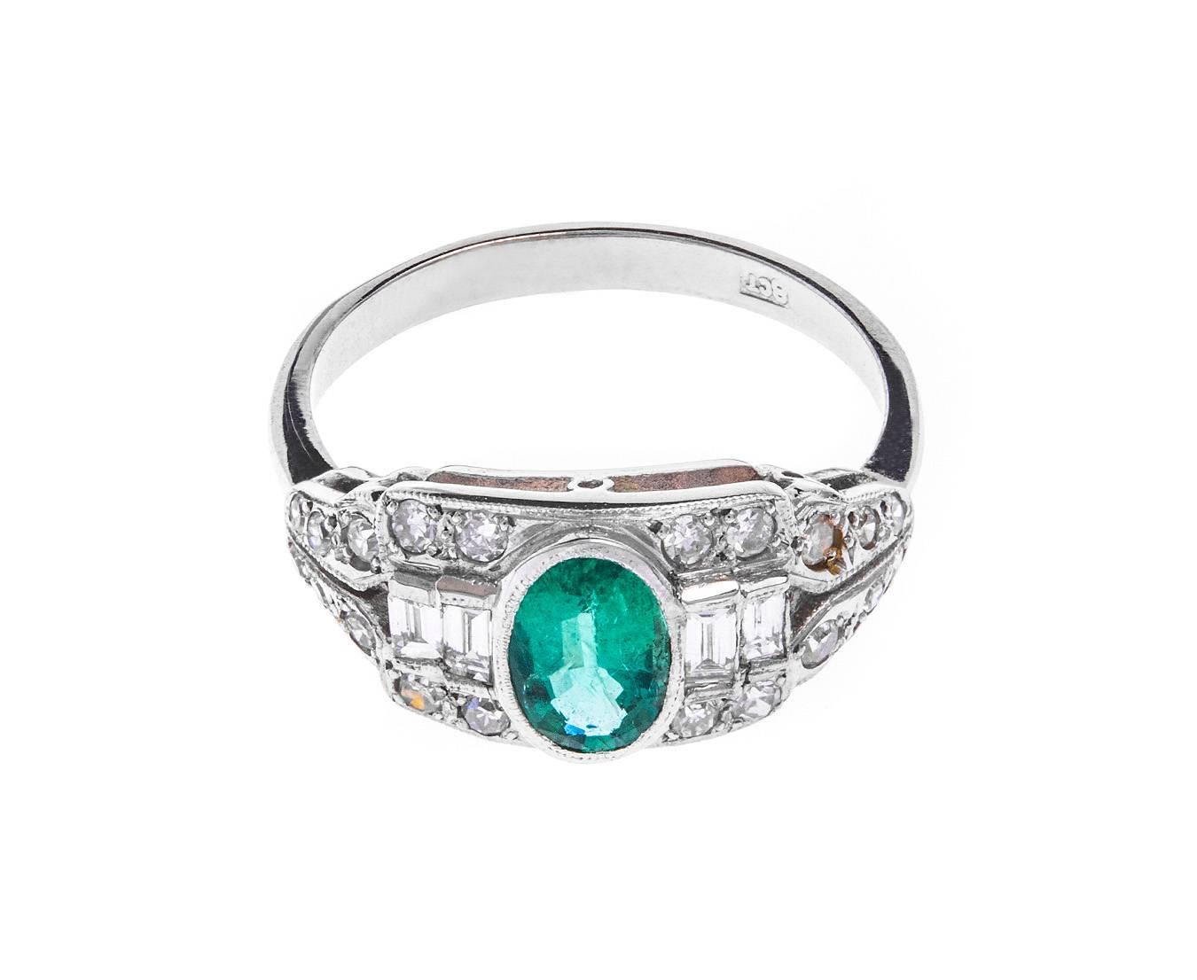 A fabulous Art Deco 18ct white gold cocktail ring, set with a deep green oval emerald amongst eight and baguette cut diamonds (estimated total 0.52ct)  in glorious geometric styles. Open gallery sides and a tapered band keep the piece light and