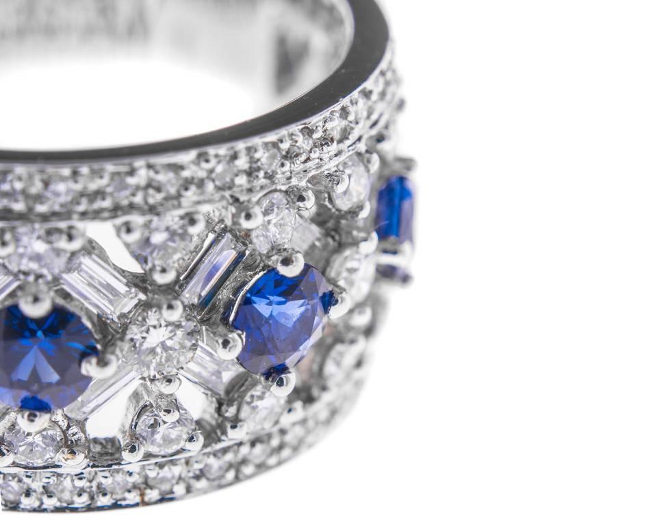 This fabulous and highly decorative dress ring is set with a vast array of sparkling diamonds creating a delicious back drop to five lush blue sapphires (0.92ct total approx) all on a wide band of white gold. It fizzes and pops with colour and
