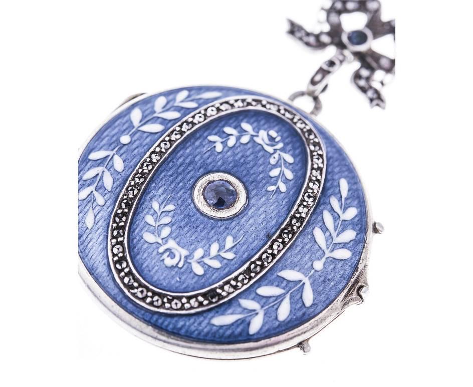 The fancy locket decorated blue guilloche enamel backdrop, with floral white enamel sides, a radiant central sapphire and marcasite accents. All The locket suspended from a fancy chain, embellished with small enamel panels.

An elegant old world