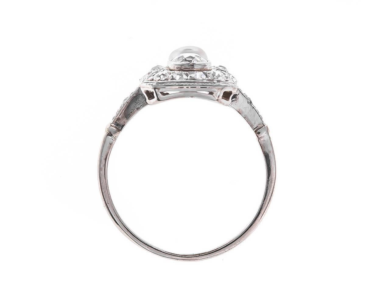 An Art Deco 14ct white gold ring encrusted with shimmering old cut diamonds around a 0.32ct old English brilliant cut diamond and gleaming white seed pearl. A plaque design measuring 15.94mm x 10.60mm, with a beautiful, finely worked gallery and