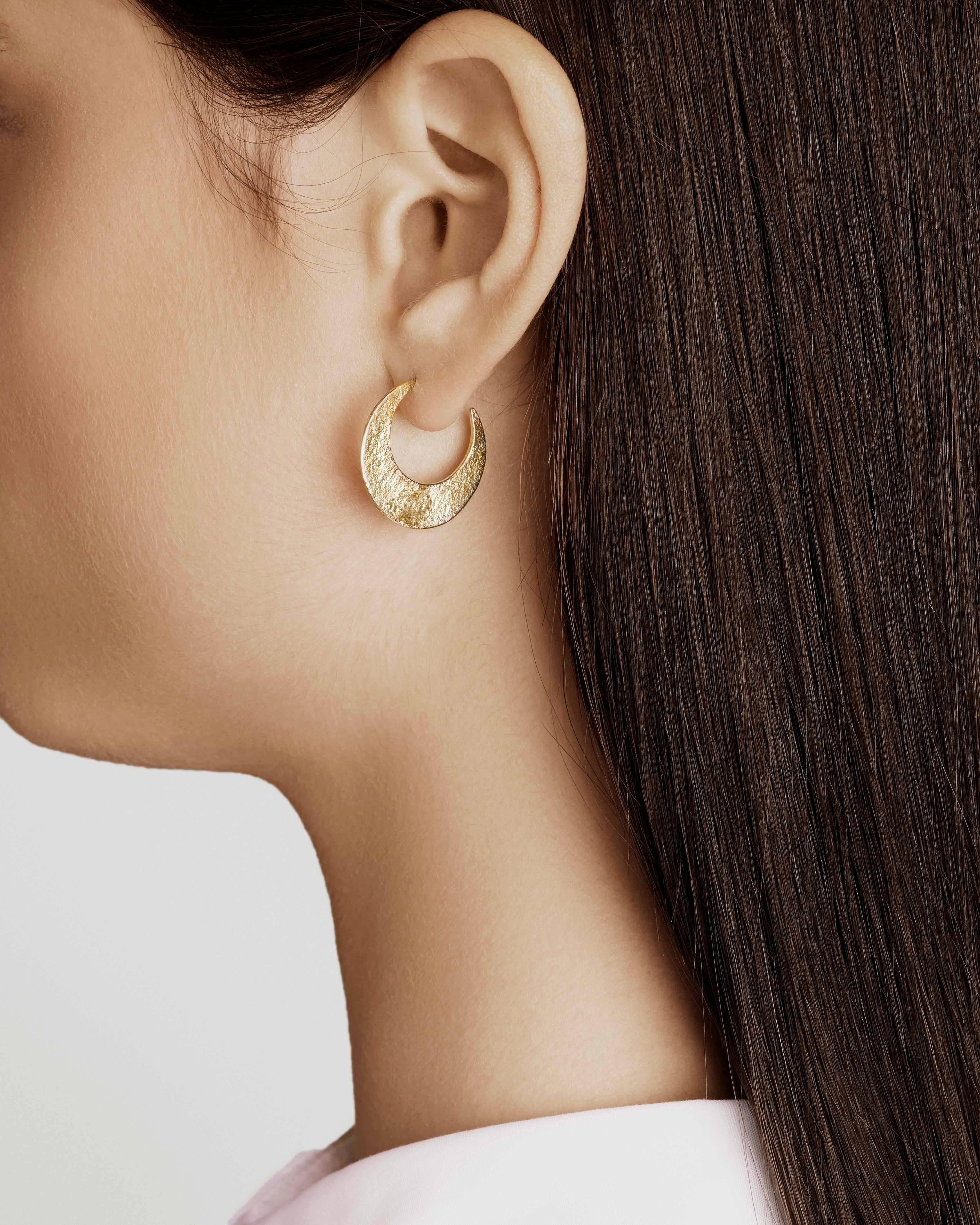 Crescent hoop earrings in 18-carat gold-plated sterling silver.  These hoop earrings feature a shimmering texture on one side and a rustic high-polish finish on the other; can be worn with either side facing out for different looks.  Hoops measure