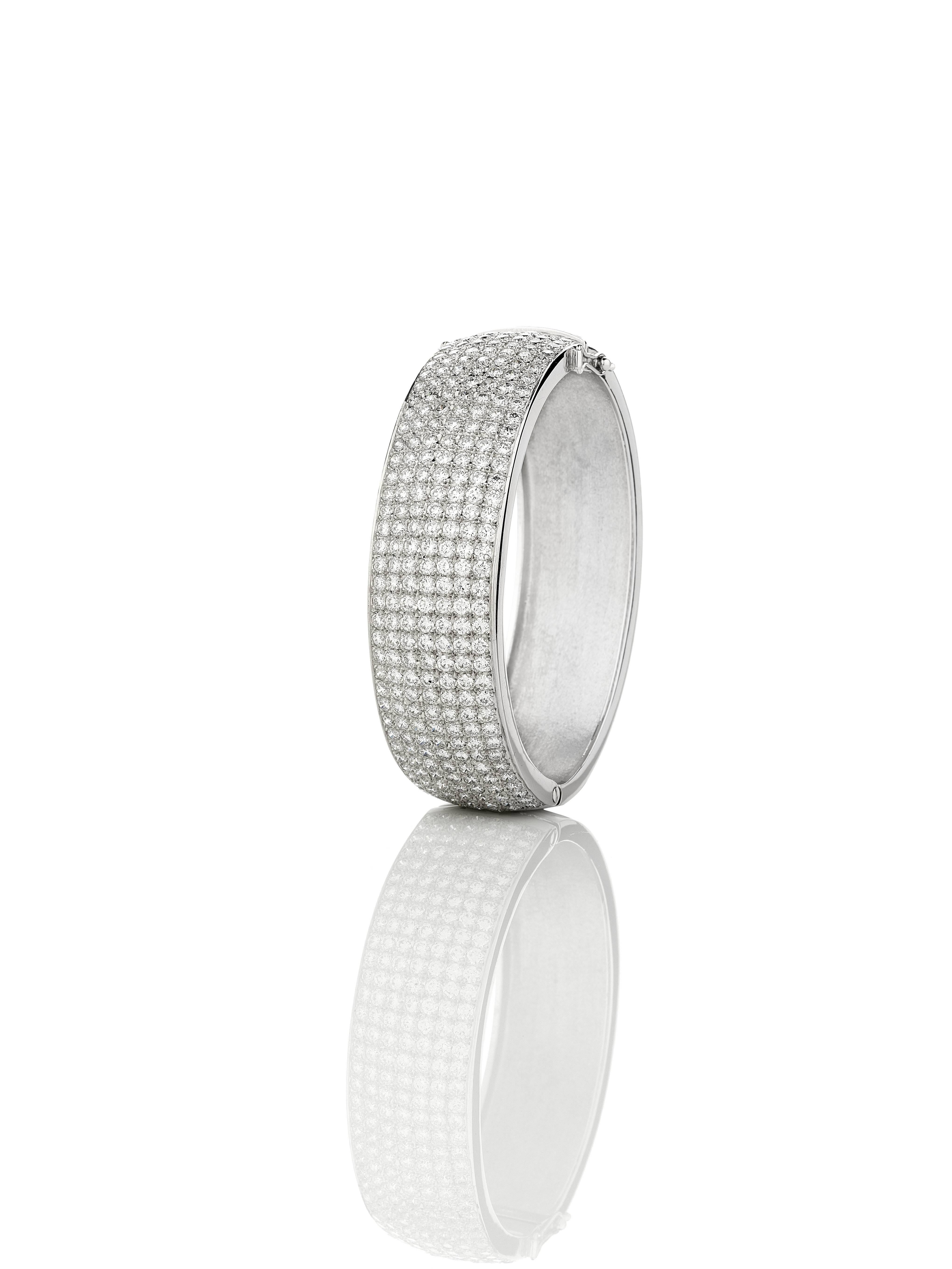 This 18kt white gold diamond pave hinged bangle is set with 252 diamonds totalling 14.00cts, G/H Colour, Si1 Clarity. The diamonds are set on the top half only with a polished back.

The bangle is 20mm wide, hinged with tongue and box clasp and two