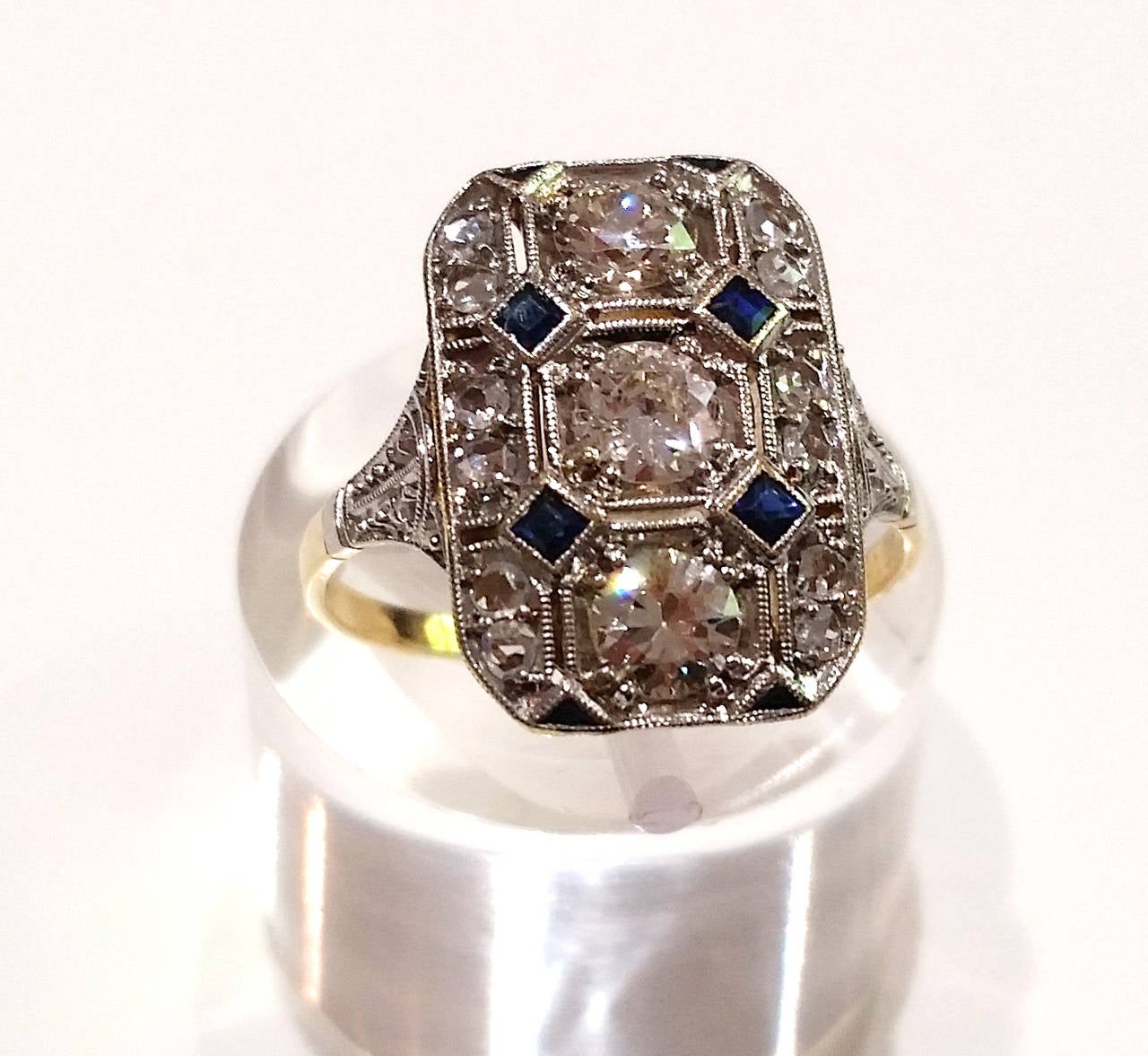Early Art Deco ring in rectangular shape, with a geometrical pattern in diamonds and blue sapphires.

18k Yellow gold and platinum.
Numbered 26673

3 Old European cut diamonds, total weight 0.75ct approx.
16 rose cut diamonds

Size: EU 14
 