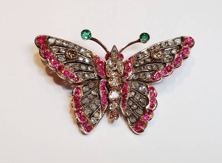 Victorian silver top with gold back butterfly brooch. Covered in old cut diamonds, with a trim of rubies and two emeralds. The body is composed of coloured diamonds