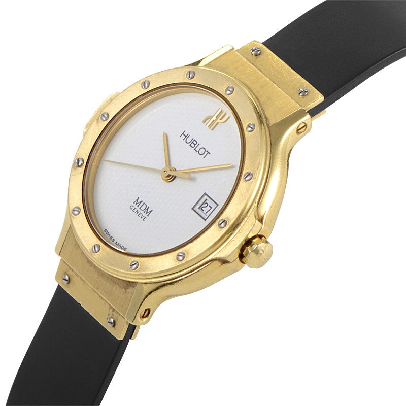 Hublot lady's 18K yellow gold quartz wristwatch on a black rubber strap. Watch indicates hours, minutes, and date on a white dial.Watch resists water to ~50m/165ft.