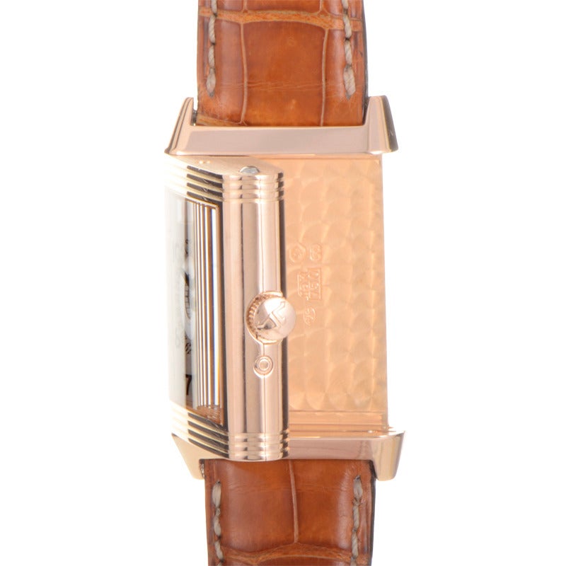 Jaeger LeCoultre 18K rose gold manually wound wristwatch on a brown crocodile leather strap. Watch indicates hours, minutes, subsidiary seconds, and day/date on a white dial with black Arabic numeral markers. Watch also has solid reversible