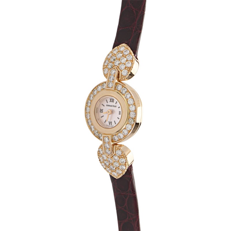 Audemars Piguet lady's 18K rose gold quartz wristwatch set with diamonds on a burgundy alligator leather strap. Watch displays indication of hours and minutes on a white dial.