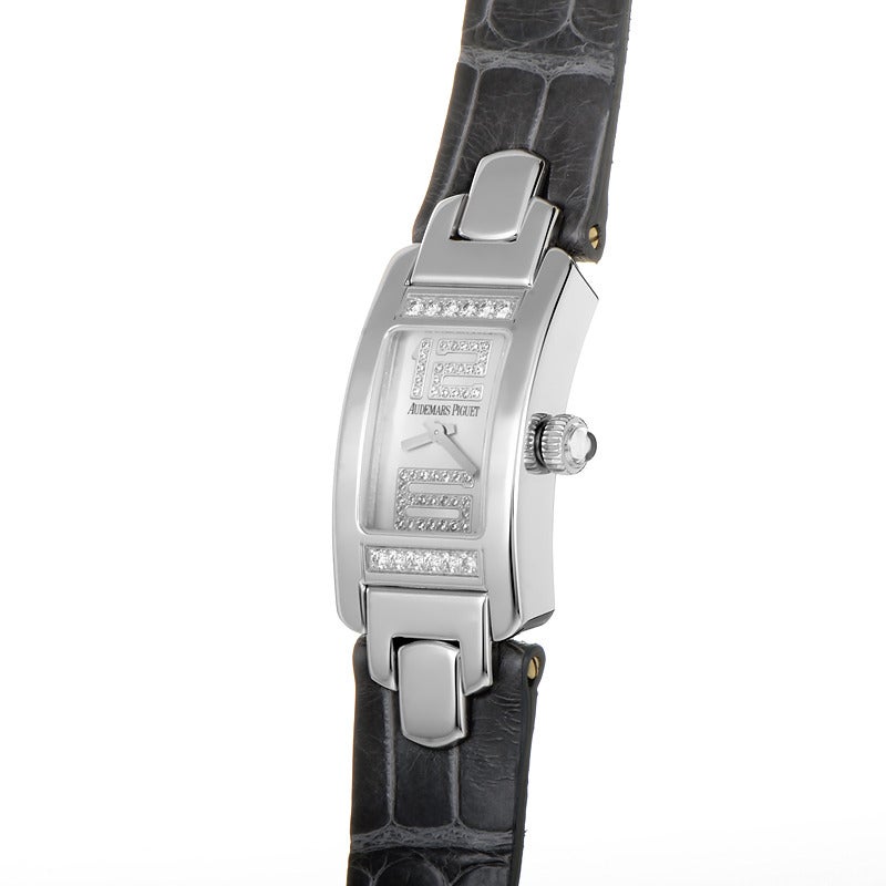 Audemars Piguet lady's 18K white gold quartz wristwatch with diamond-set bezel on a dark gray leather strap. Watch displays indication of hours and minutes on a mother of pearl dial with two diamond-set hour markers.