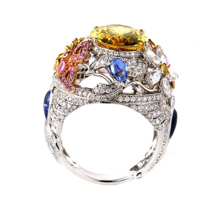 The sumptuous design of this Garrard ring is truly a delight. This elegant 18K white gold ring features floral shaped motifs, some of which are made of yellow or rose gold. The flowers are set with multi-colored sapphires and are accented with a