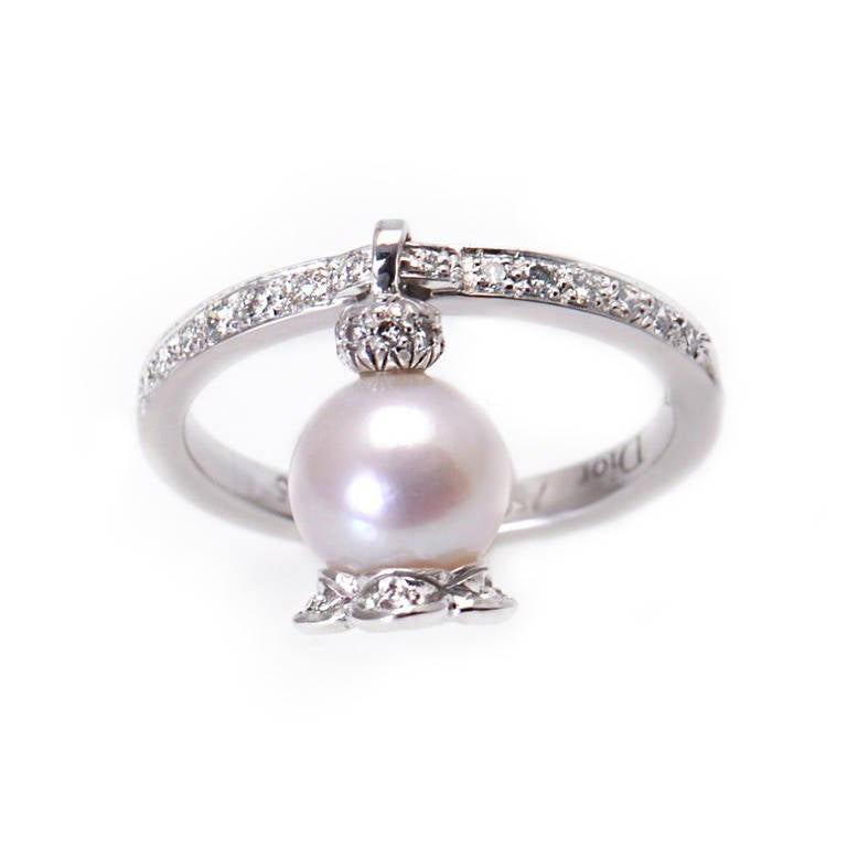 Fabulous ring in 18K white gold from Dior has all the right elements. The top of the band is set with diamonds and rises to a loop in the gold which has a pearl that dangles from it.The pearl has circles of pave diamonds set around the top and the