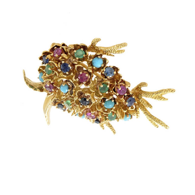 Playful and pretty, this lavishly designed fish is perfect for the lady who likes to shine! The brooch is made of textured 18K yellow gold and is shaped like a fish. The brooch is studded with ~.35ct of rubies, ~.35ct of sapphires, ~.30ct of