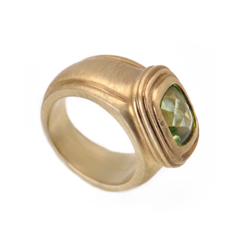 Slane & Slane 18K yellow gold medium rectangular ring encompassing all the iconic design elements - brushed matte yellow gold forms a wide band . 
The setting is slightly raised and features a smooth peridot stone in a wonderful shade of