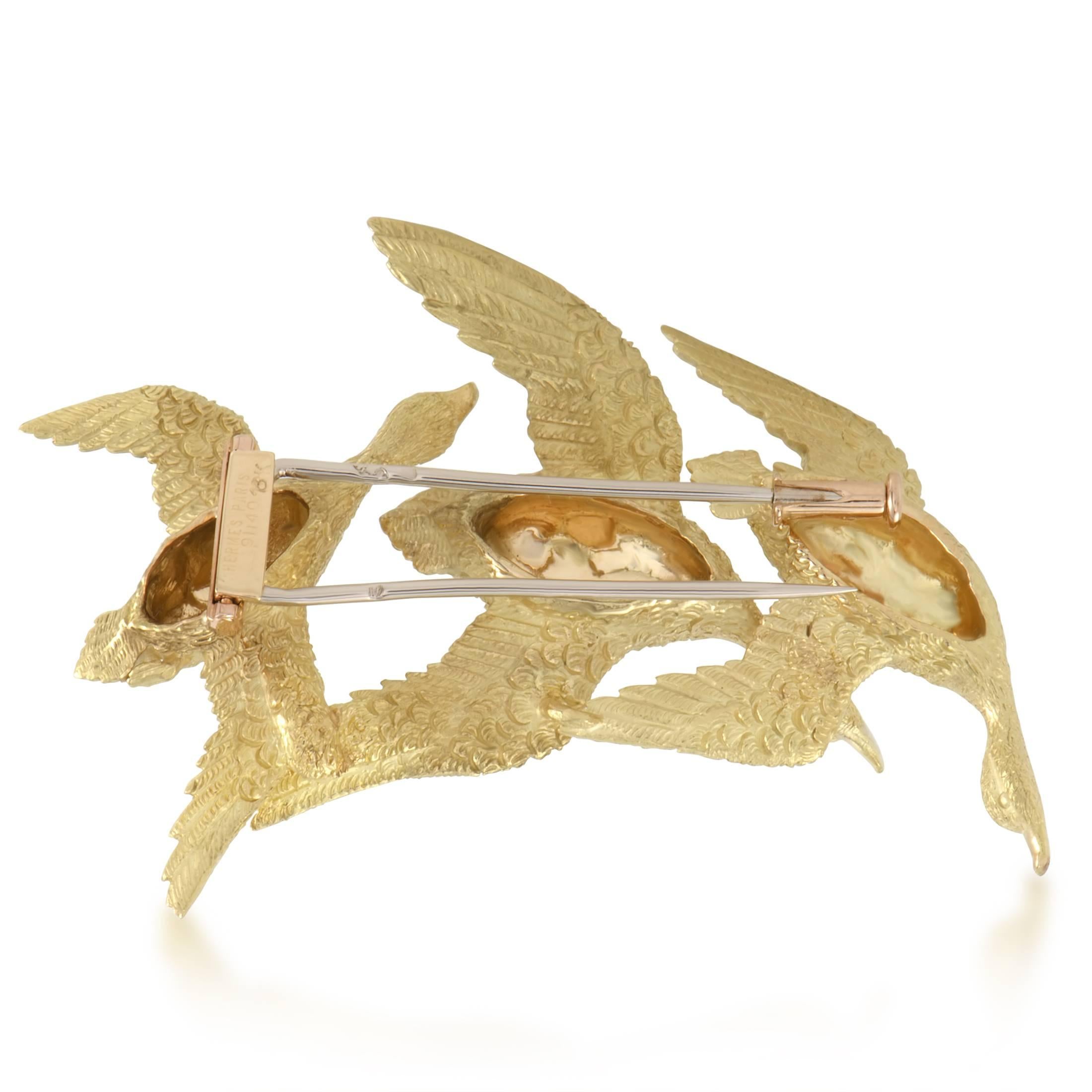 Amazingly intricate finish and luxurious intrinsic radiance of 18K yellow gold produce an enchanting visual effect in this majestic brooch from Hermès designed in the form of graceful birds with piercing eyes of precious sapphires for a nifty final