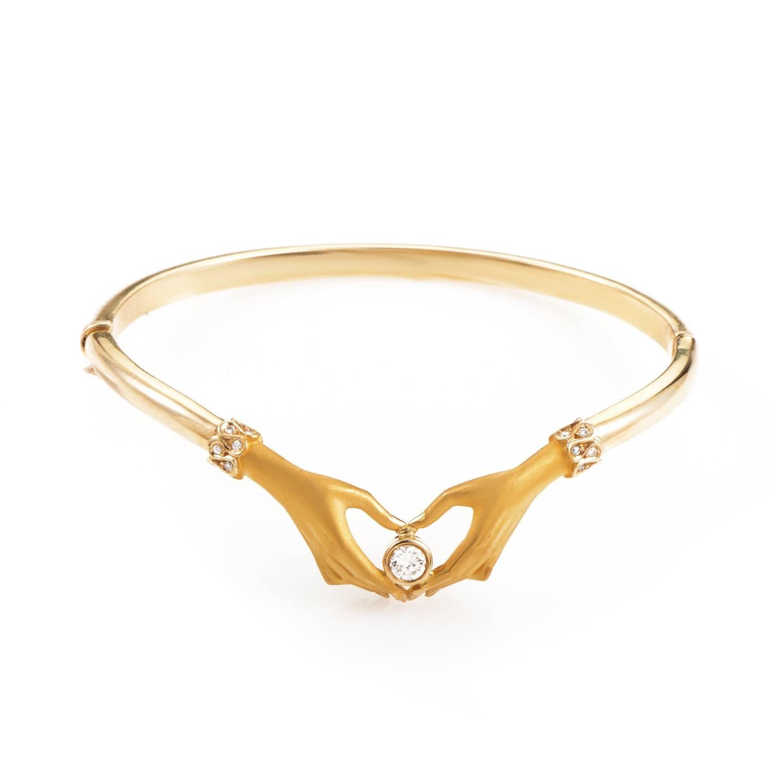 This gorgeous bangle from Carrera y Carrera is absolutely breathtaking. It is made of 18K yellow gold and features two dainty hands cupping an exquisite diamond. Both hands are accented by small diamond 