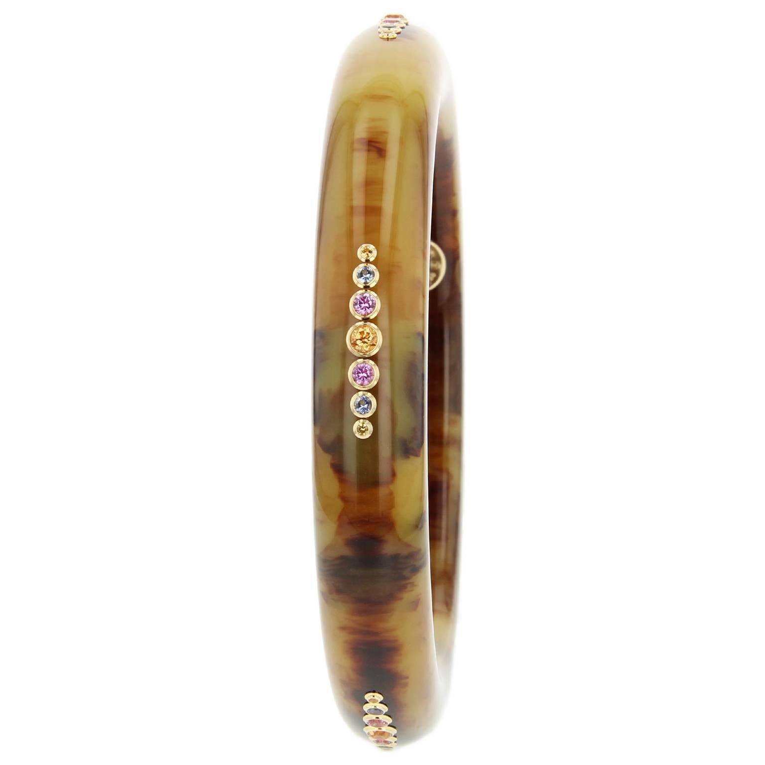 This thin Mark Davis bangle was handcrafted using marbled brown vintage bakelite. Studded with five evenly spaced graduated sections of blue, yellow and pink sapphire centered with spessartite garnet, all bezel-set in 18k yellow gold. 

Full details