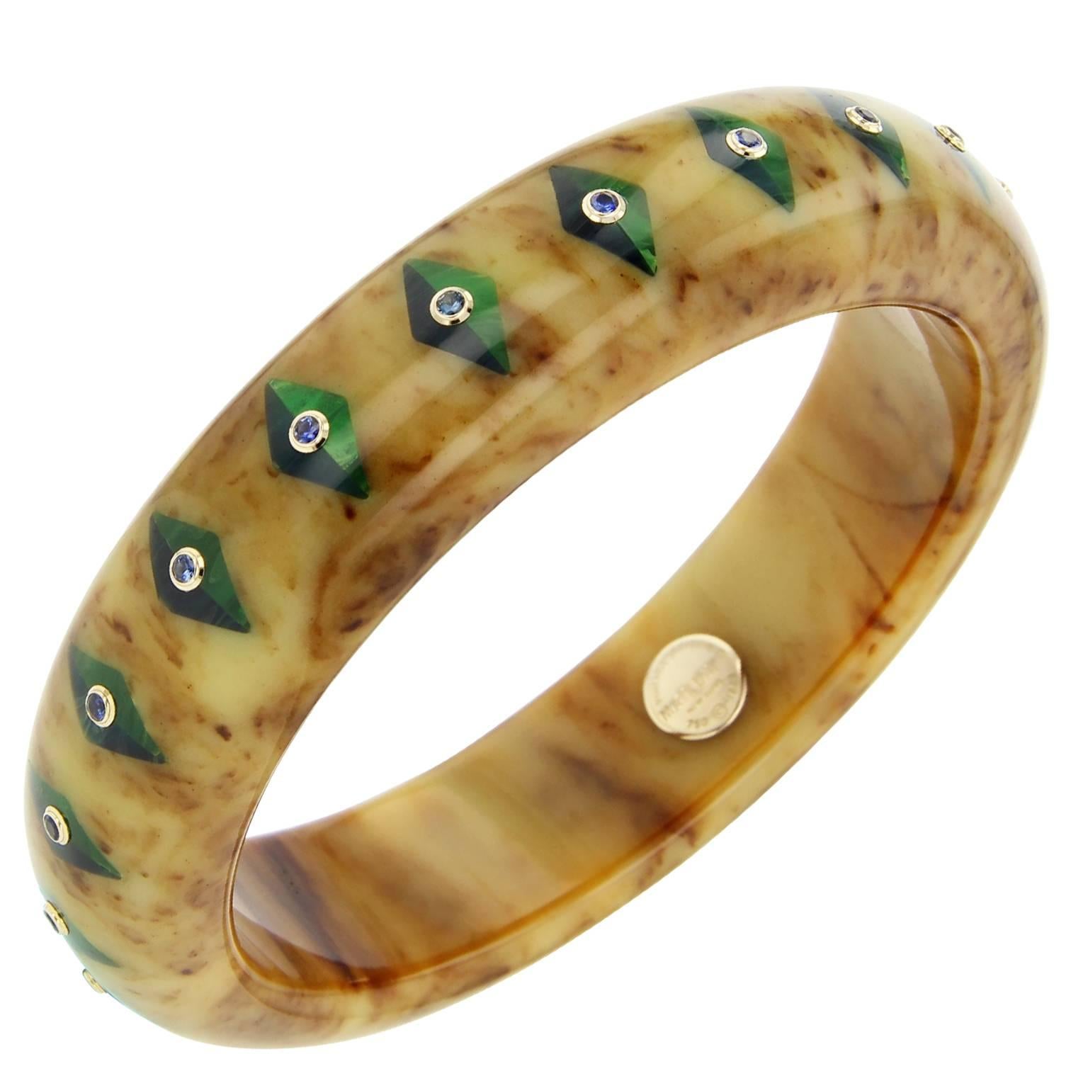 This chic Mark Davis bangle is handcrafted using marbled brown vintage bakelite. Precisely inlaid with a diamond-shaped motif of half blue and half green lozenges and studded with fine blue sapphires, bezel-set in 18k yellow gold.

Full details
