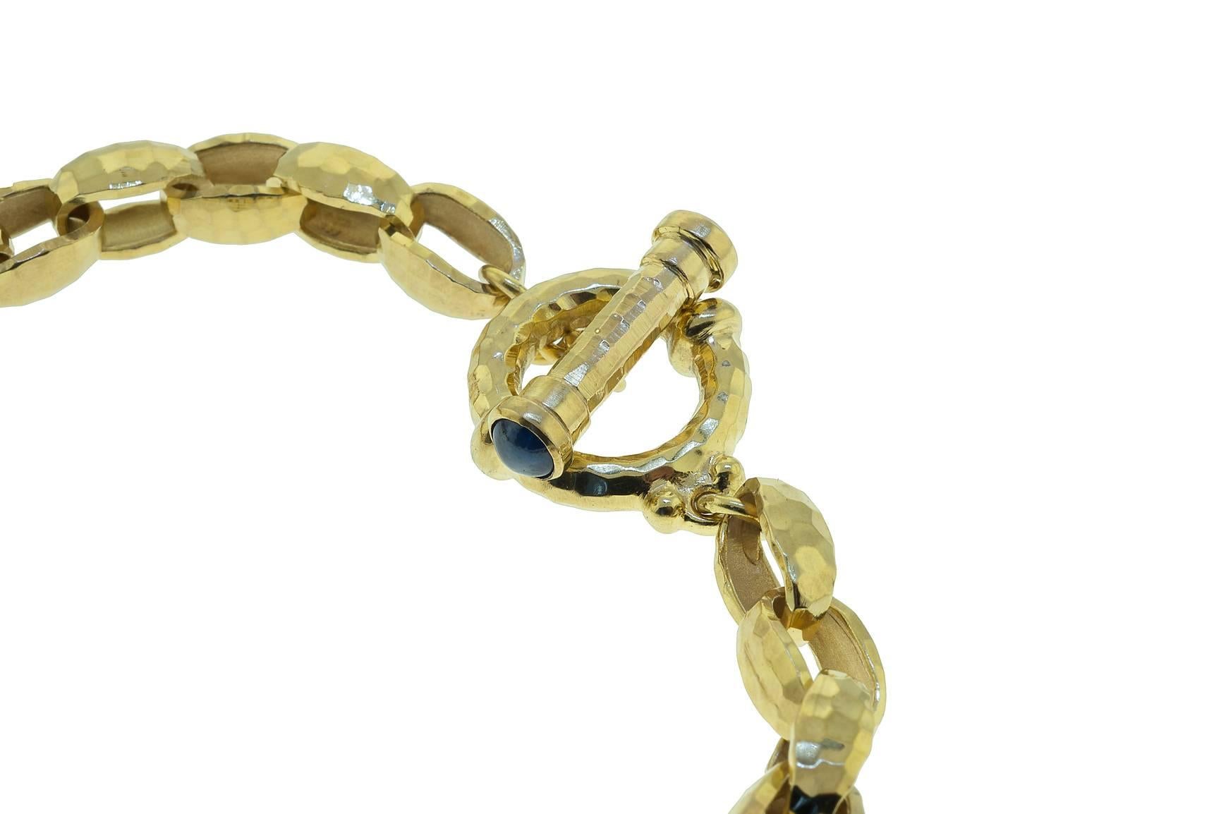 14K yellow gold oval link toggle bracelet. The links are oval and have a hammered finish. The toggle has sapphire cabochon on each end.
