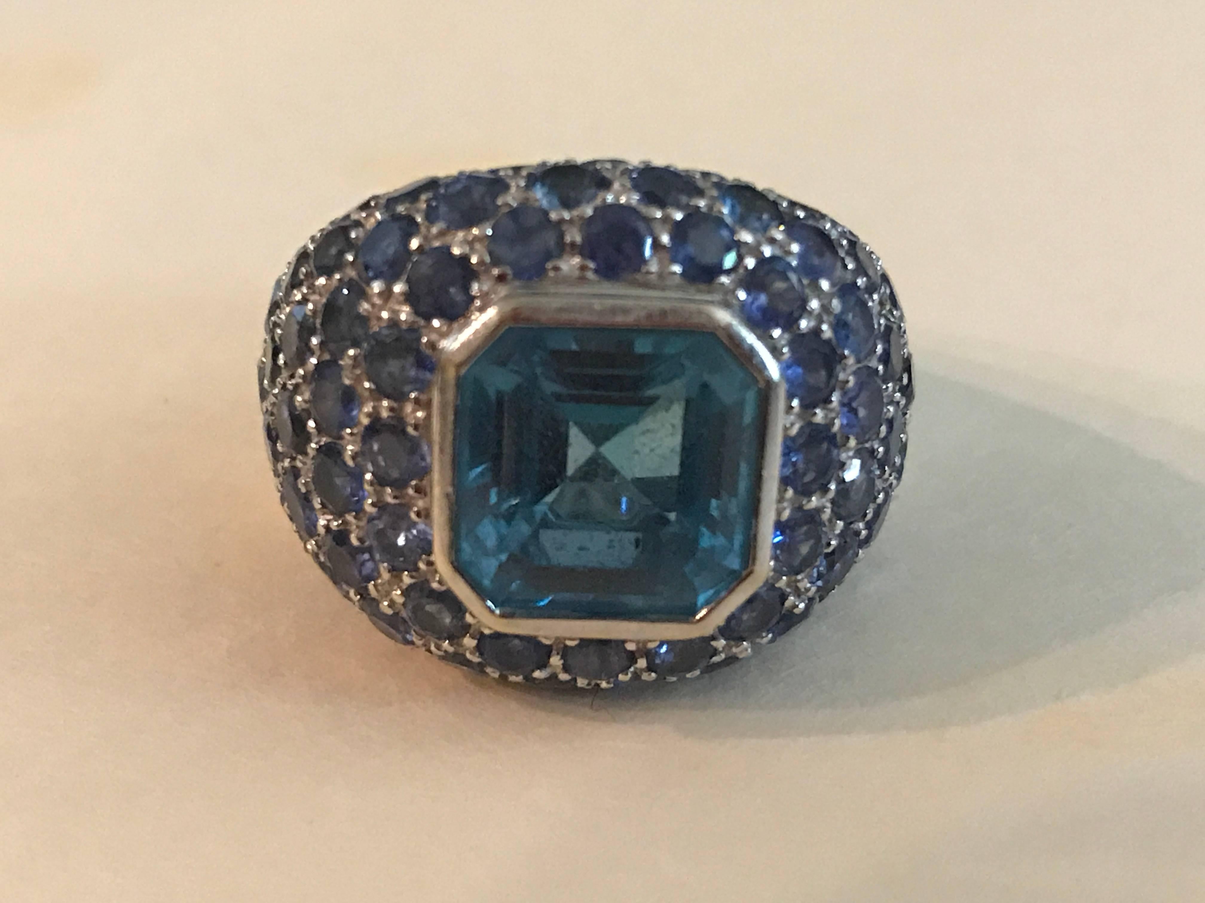 18K white gold dome ring with a bezel set blue topaz in the center. The mounting contains pave set blue sapphires. 
