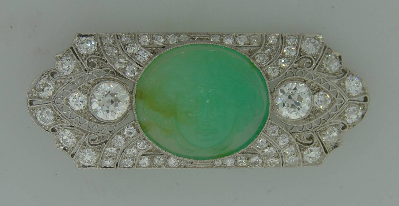 Gorgeous Art Deco pin created in the 1920's. Features an oval carved jade centered in a platinum and diamond frame. The diamonds are of Old European cut, the two biggest diamonds are approximately 0.65 carat each. Diamond total weight is 3.58