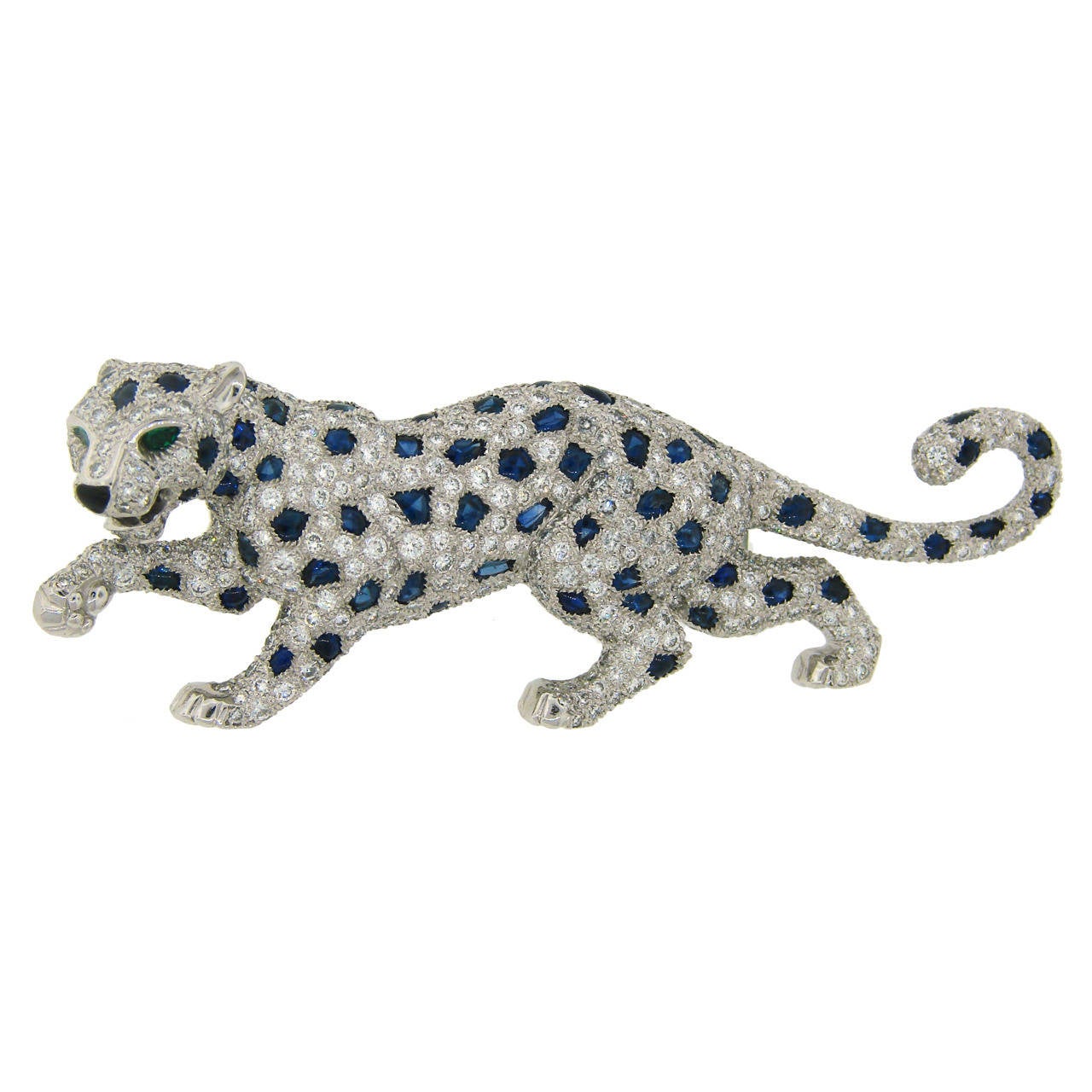 Signature Cartier Panthere brooch. 
Made of platinum and set with round brilliant cut diamonds and sapphires. The panther eyes are accented with emeralds. 
The pin is 2-3/4