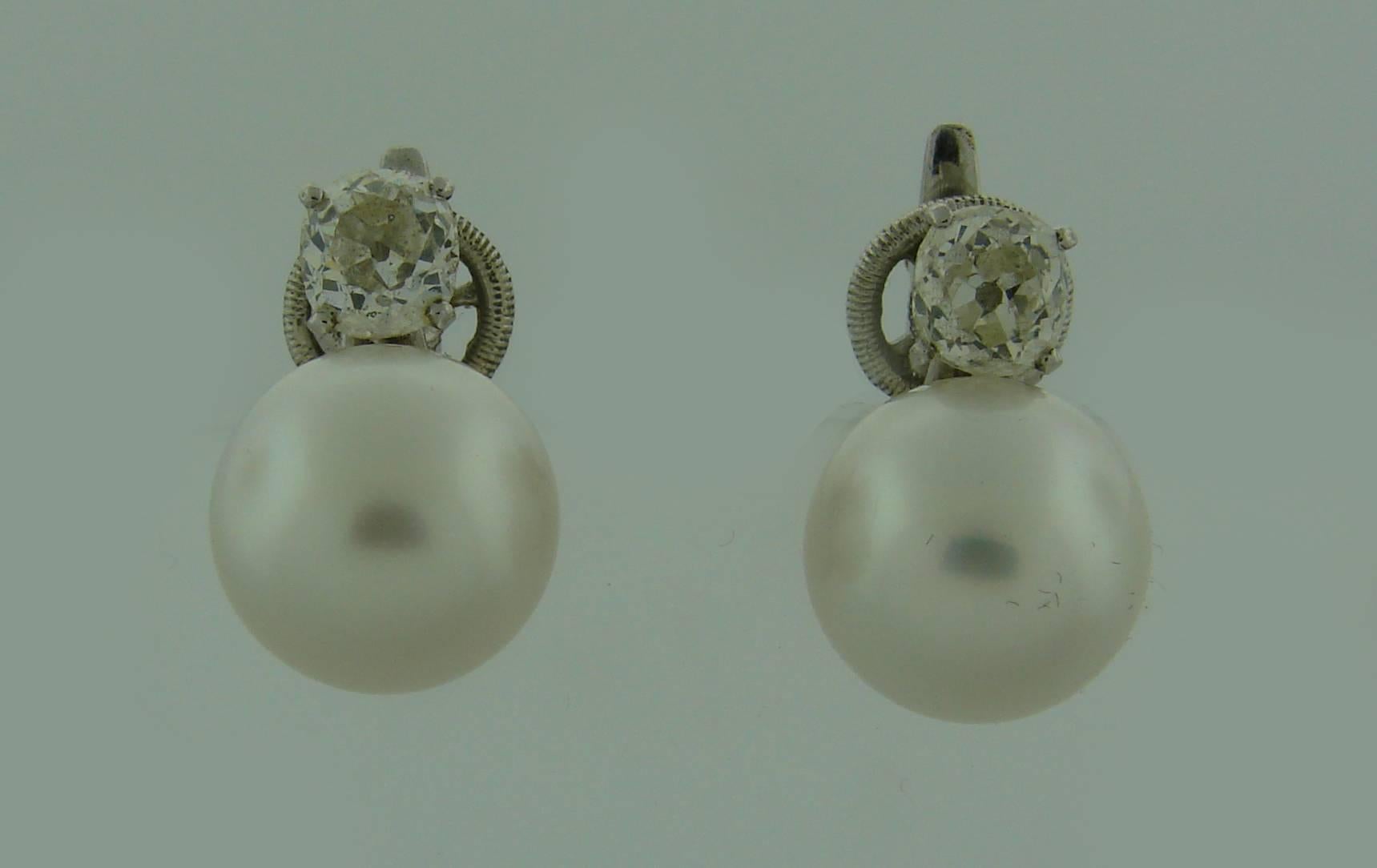 Elegant and timeless earrings featuring two beautiful pearls and two old cushion cut diamonds mounted in 18k (tested) white gold by Cartier. 
The pearls are white with nice luster and measure approximately 10.77 mm and 10.82 mm in diameter. The