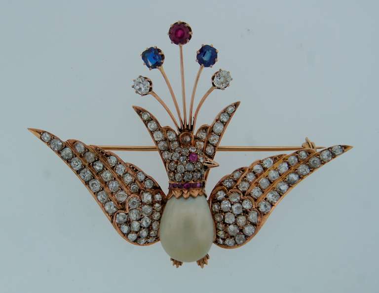 Adorable peacock brooch created in the beginning of 20th century. Definitely a conversational piece!
Made of rose gold, features a natural drop shape pearl, encrusted with old mine and cushion cut diamonds, rubies and two sapphires. The pearl comes
