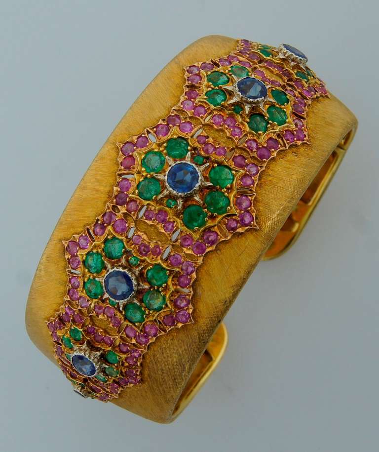Famous signature Buccellati bracelet created in Italy in the 1970's. The highlights of this bangle are typical Buccellati satin finish on a gold and ornamental design encrusted with sapphires, rubies and emeralds.

The bangle is 1-1/8