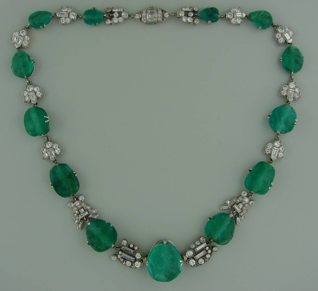 Stunning Art Deco set featuring sixteen carved emeralds set in platinum and accented with Old European cut and baguette cut diamonds. 
The necklace has thirteen graduating drilled carved emeralds, the center one measures 15.24 x 16.97 x 10.12 mm and