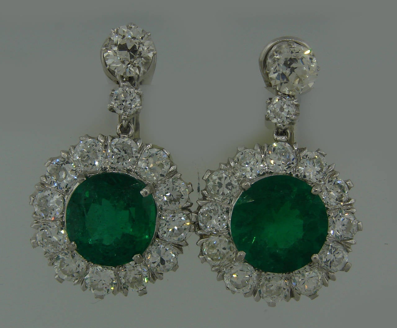 Magnificent dangle earrings created in the 1930's. Feature two natural Brazilian emeralds about 5 carats each set in platinum and surrounded with twenty eight Old European cut diamonds - total weight 3.28 carats. The emeralds are round faceted and