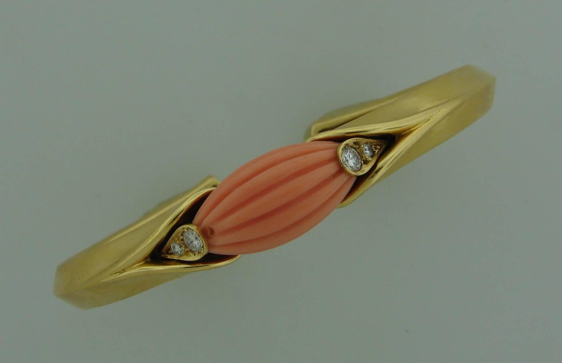 Elegant and classy bangle created by Van Cleef & Arpels in France in the 1971. Features a carved coral set in 18k yellow gold and accented with round brilliant cut diamonds. 
The bracelet fits up to 6.5