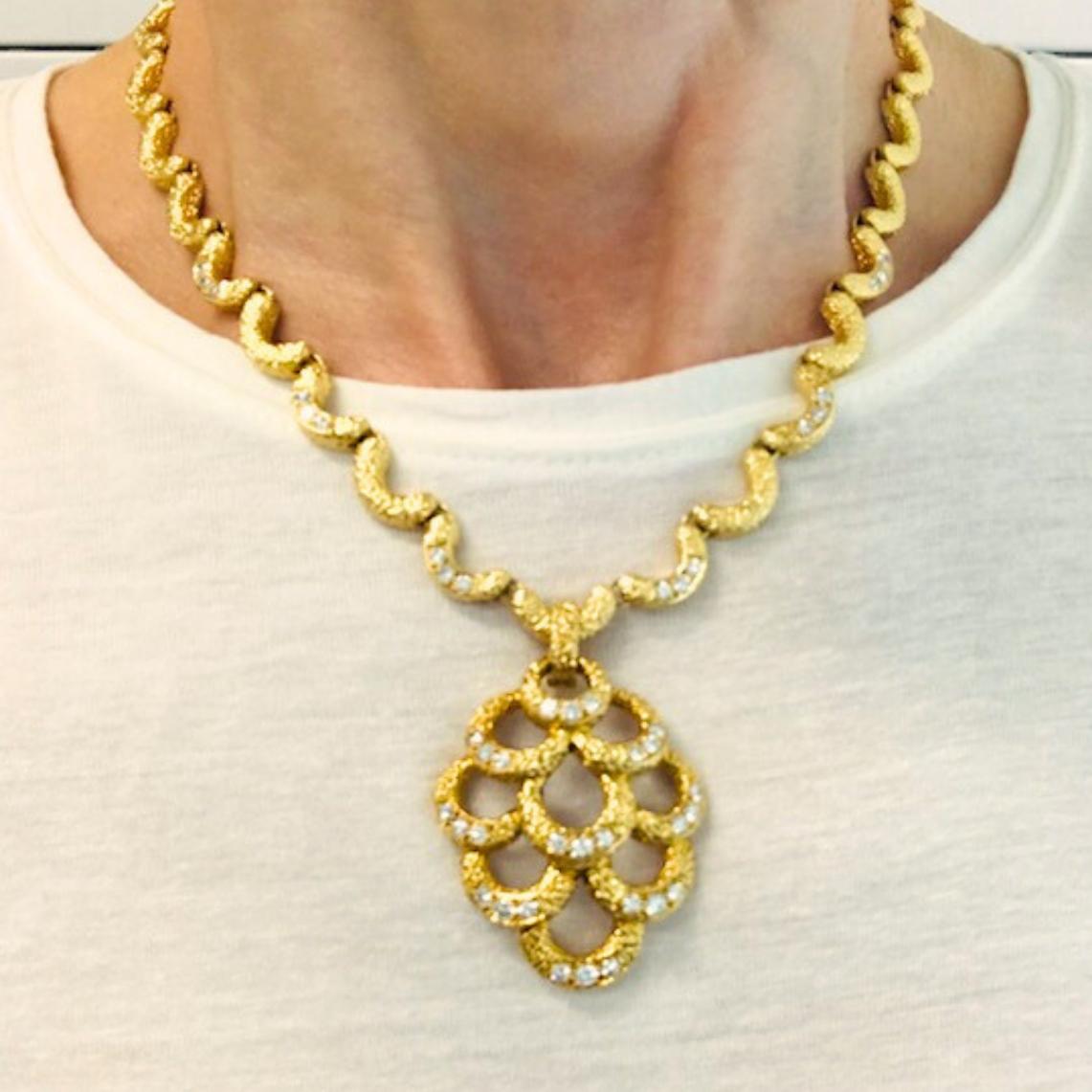 Realizzata in oro giallo 18 carati, questa collana vintage di Fred Paris presenta un caratteristico design a smerlo con una texture opaca. Molti dei segmenti smerlati sono punteggiati da diamanti rotondi a taglio brillante. 
Al centro è sospeso un