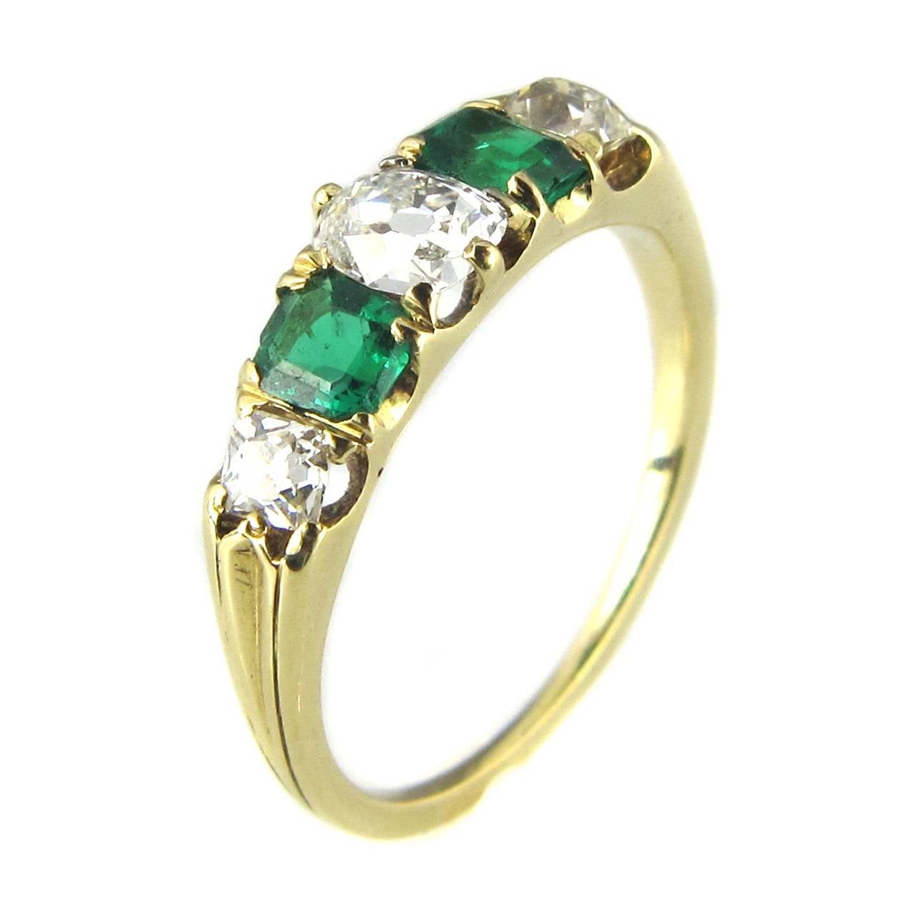 An antique late Victorian five stone emerald and diamond ring, comprising three graduated old cushion cut diamonds, estimated to weigh0.90 carats in total and two emerald-cut emeralds, estimated to weigh 0.50 carats.  The stones are claw set in an