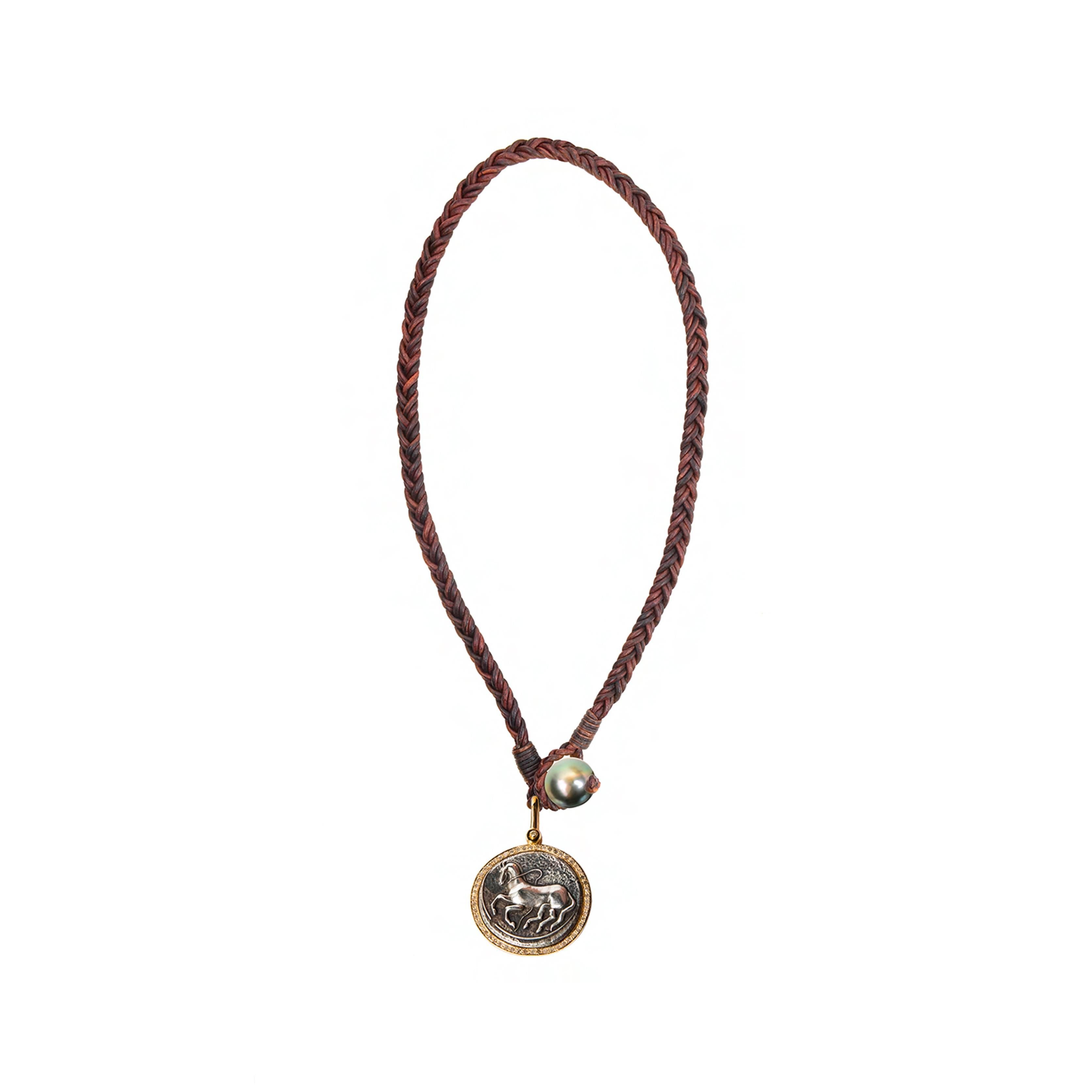 Trojan Coin Necklace with premium braided brown leather cord, designed by American Designer, Vincent Peach. This necklace has Sterling Silver Trojan coin encircled by 10k Yellow Gold bezel and a Tahitian Pearl and loop closure.  Standard 17 inches