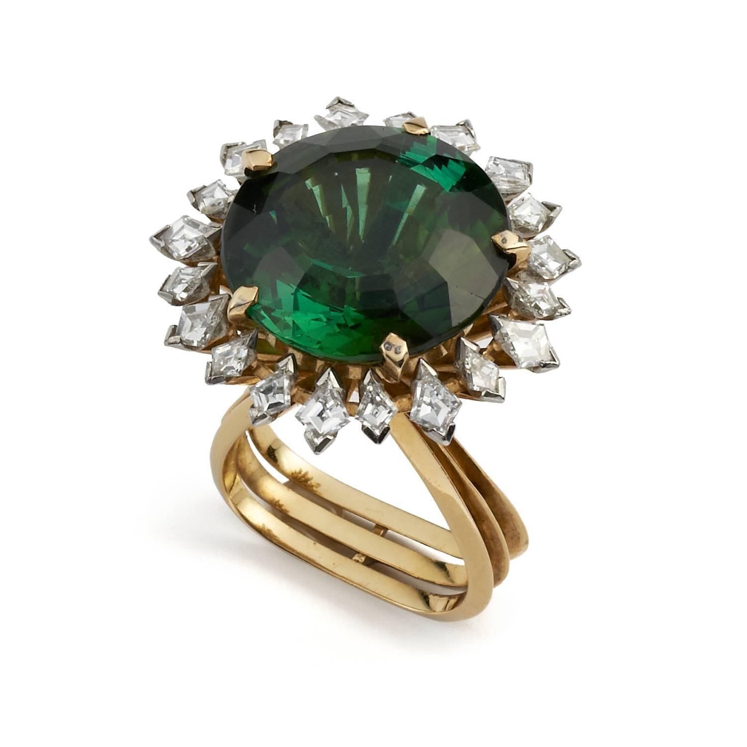 Designed by Andrew Grima in 1974
A superb and rare circular green tourmaline (23cts) is skillfully held by twenty kite-shaped diamonds of varying sizes in platinum. The diamonds in collets are mounted on stalks of yellow gold. Signed GRIMA, London