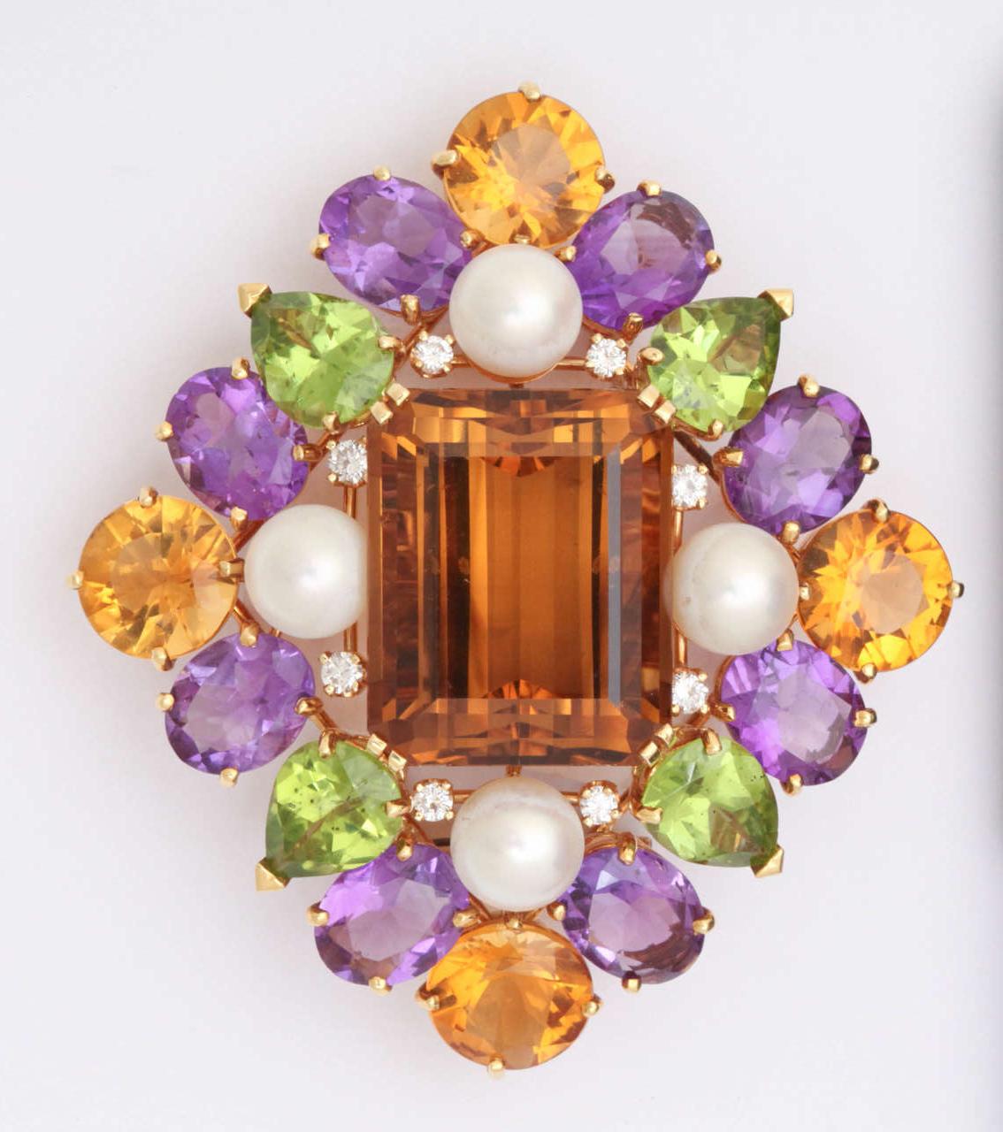 This regal pin has a central emerald cut citrine, measuring  3/4 inches by 1 inch, surrounded by pear-shaped peridots, oval amethysts and round citrines. To set off the colored stone are four round cultured pearls and eight 5-point diamonds. The