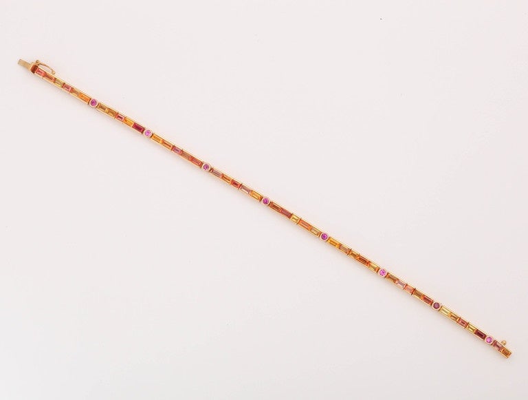 This bracelet is a classic 'line' bracelet where the stones are set flexibly in a straight line. The sapphires  are baguette cut ,light to darker orange with round pink sappires interspersed. It is made in 18 kt orange gold and has a secure lock and