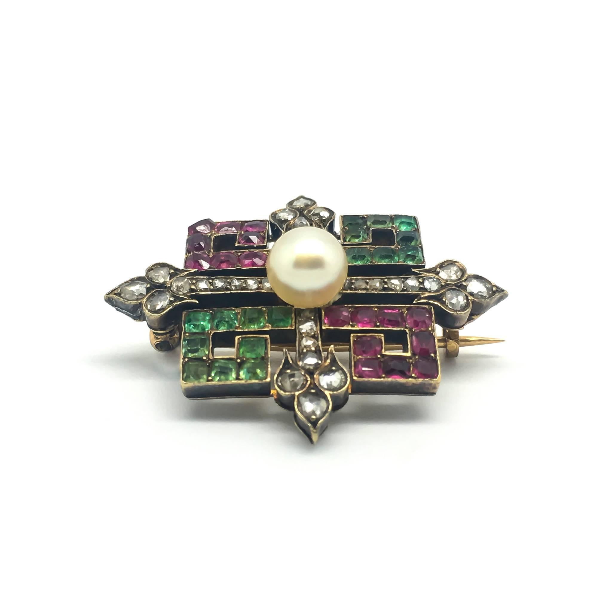 A fine Victorian Brooch set with emeralds, diamonds, sapphires and a central pearl.

The brooch contains a cross motif with geometric shapes around it. The calibre set stones are vibrant and well matched throughout. 

The brooch fitting is on a