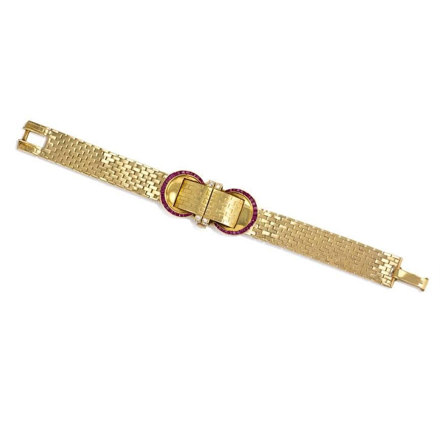 A Retro covered gold bracelet watch on a brick-link strap with a shuttered face flanked by circular ruby and diamond embellishment, in 18K.  John Rubel Co.
