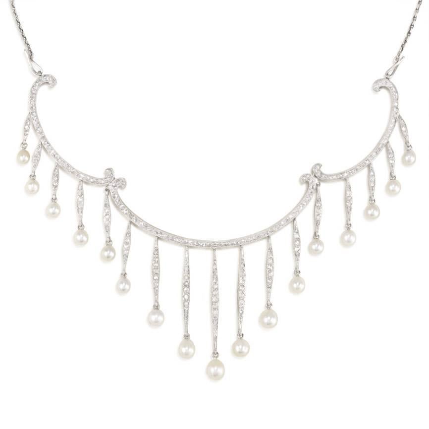 An Edwardian pearl and diamond fringe necklace comprised of three scrolled swags, in platinum. Koch, Austria