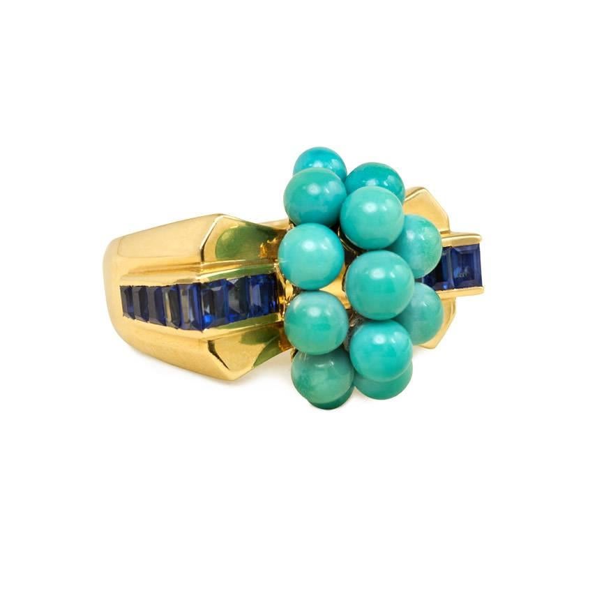 A Retro gold, turquoise, and sapphire ring of stylized bow design, the center beaded cluster of turquoise flanked on both sides by a row of calibré sapphires, in 18k.  Mauboussin, Paris
Center: 17mm high, 2.3cm wide
