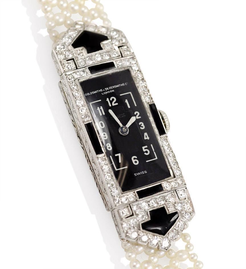 An Edwardian diamond, onyx and natural seed pearl wristwatch with a black enamelled face, in platinum.  Retailed by Goldsmiths & Silversmiths Company (forerunner to Garrard & Co.); movement by Vacheron Constantin # 405231.