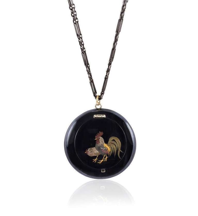 An antique black enamel vanity case pendant with a mixed metal rooster motif on a gun metal chain.